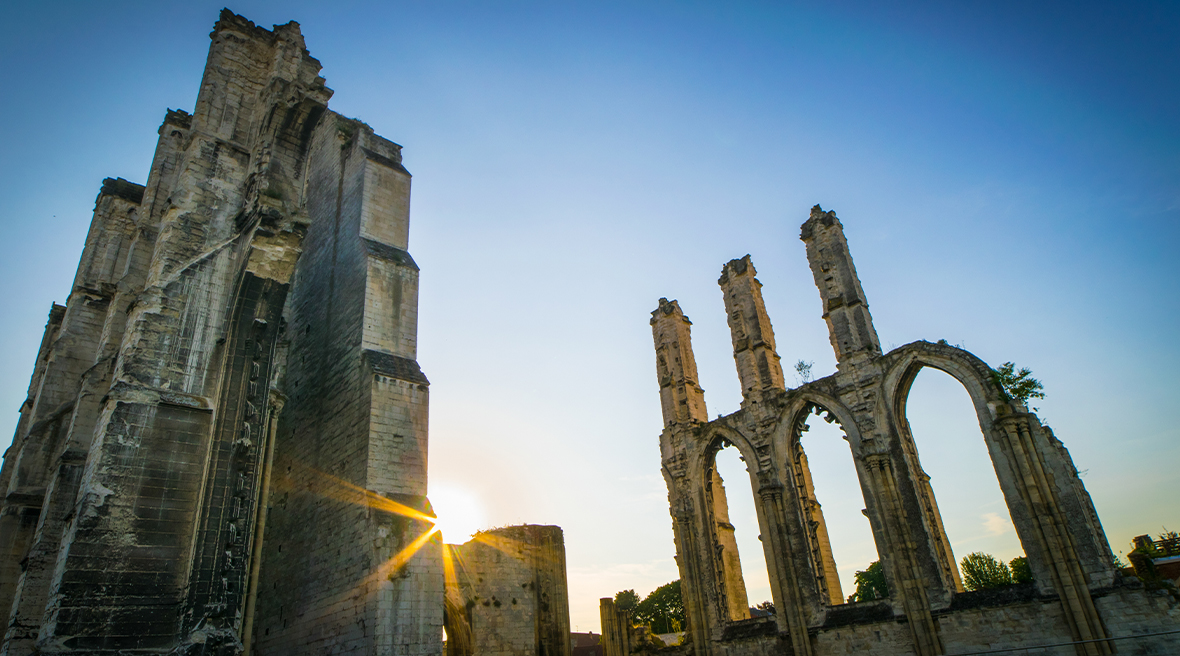 The ruins of a religious building at dusk or dawn, as the sun’s rays are glimpsed low in the cloudless blue sky